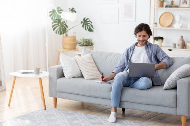 Dizüstü bilgisayarı olan genç bir adam, ev içi notlar alıyor.