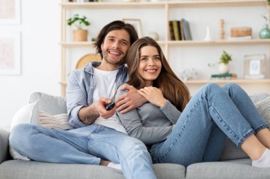 Evde birlikte televizyon izleyen neşeli genç bir çift.