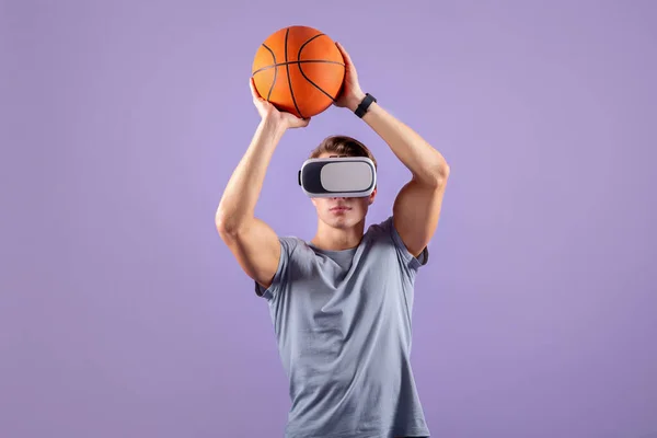 Virtueel sportconcept. Jonge gespierde man basketbal spelen terwijl het dragen van VR headset op violette studio achtergrond — Stockfoto
