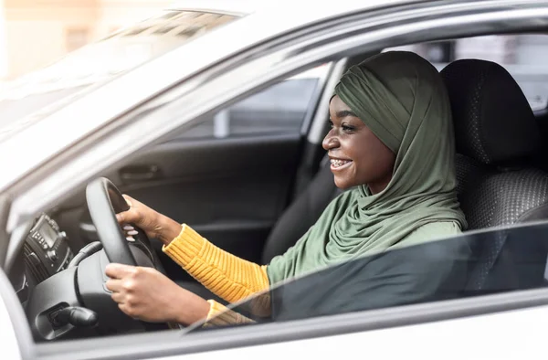 Vrolijke Afrikaanse moslim dame in hoofddoek autorijden in de stad, zijaanzicht — Stockfoto