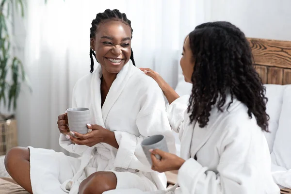 两个穿着浴衣的年轻妇女坐在床上喝咖啡 — 图库照片