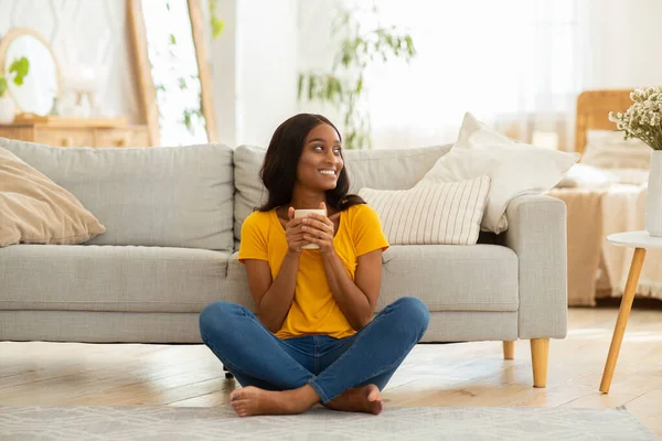 Retrato de larga duración de una joven mujer negra tomando café en el suelo cerca del sofá en casa —  Fotos de Stock