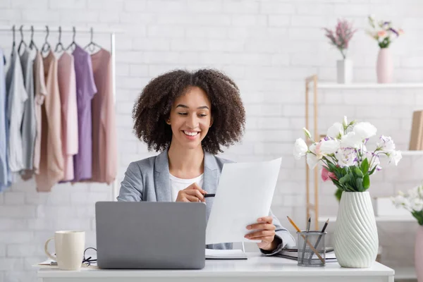 Goede opstarten en de resultaten van de verkoop van kleding in online winkel tijdens zelf-isolatie thuis. Gelukkig Afrikaans amerikaanse dame in business suit werken met documenten — Stockfoto