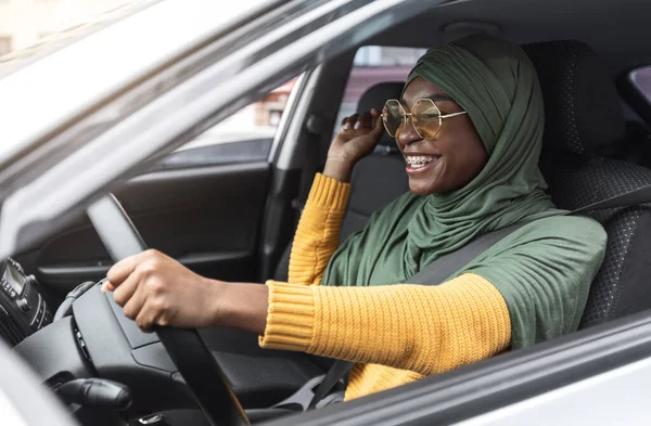 첫 번째 차량. 히잡 에서 새로운 자동차를 운전하는 쾌활 한 젊은 흑인 회교도 여인 — 스톡 사진