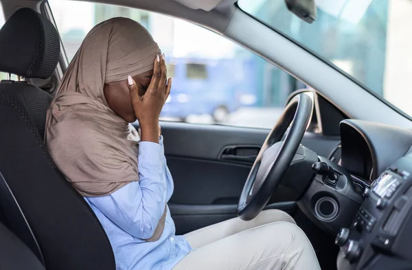 Stressed black muslim woman driver sitting in car, covering face with hands