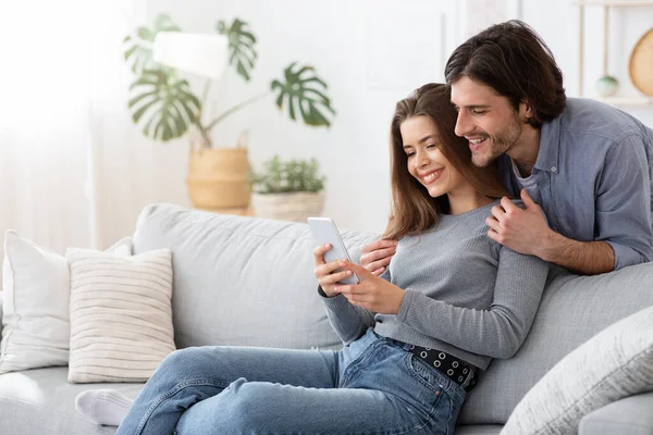 Pareja joven positiva usando teléfono móvil en casa — Foto de Stock