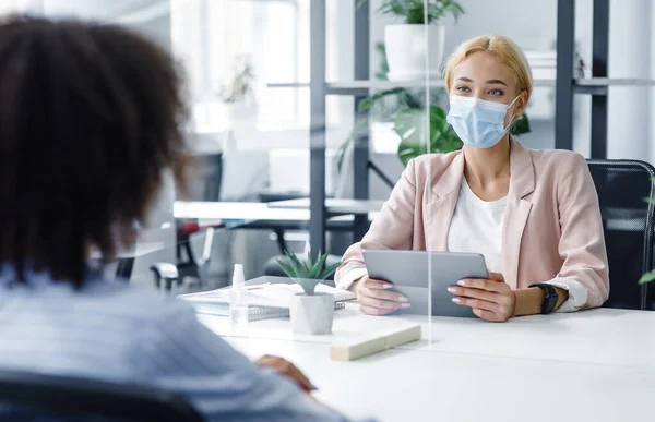 New normal and modern interview during covid-19 outbreak. HR manager with laptop looks at african american woman through protective glass