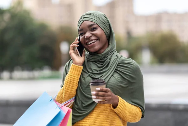 Dışarıda cep telefonuyla konuşan, alışveriş torbaları ve kahveli siyahi Müslüman kadın. — Stok fotoğraf
