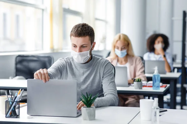Coronavirus quarantine and office work with colleagues keeping social distancing. Portrait of young man in protective mask make video call with client — Stock Photo, Image