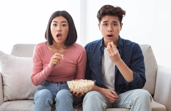 Σοκαρισμένο ασιατικό ζευγάρι βλέποντας τηλεόραση τρώει ποπ κορν κάθεται στο σπίτι — Φωτογραφία Αρχείου