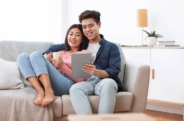 Casal asiático usando tablet digital sentado no sofá em casa — Fotografia de Stock