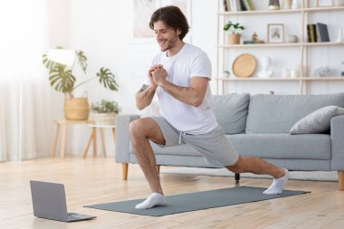 Neşeli sporcu adam evde egzersiz yapıyor, dizüstü bilgisayar kullanıyor.
