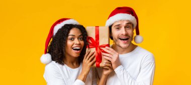 Noel Baba şapkalı heyecanlı bir çift Noel Baba 'nın hediye kutusunu taşıyor.