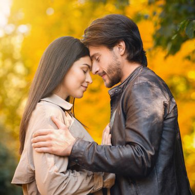 Birbirine aşık çiftler sonbahar ormanı geçmişinde kucaklaşıyorlar.