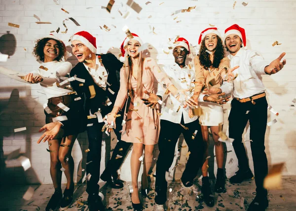 Uomini e donne che festeggiano il Natale in piedi sotto la caduta Confetti Indoor — Foto Stock