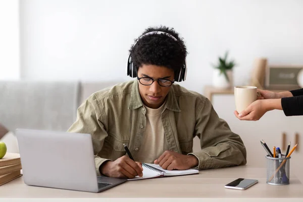 Negro adolescente chico en auriculares estudiar en línea desde casa, tomando notas en copybook — Foto de Stock