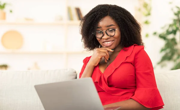 Sorrindo mulher negra sentada no sofá com seu laptop — Fotografia de Stock
