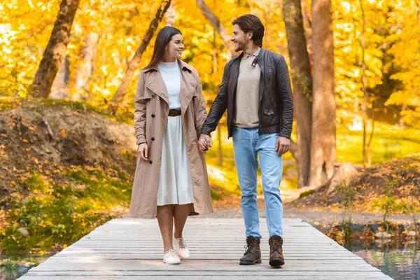 Jóvenes amantes alegres tomados de la mano y caminando por el parque —  Fotos de Stock