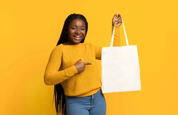 Cheerful Black Lady Pointing At Blank Tote Canvas Bag In Her Hand