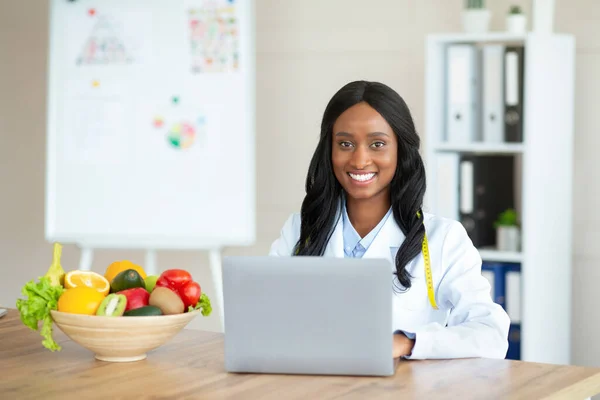 Χαρούμενη μαύρη γυναίκα διαιτολόγος με φορητό υπολογιστή συμβουλεύεται ασθενή σε απευθείας σύνδεση στην κλινική, κενό χώρο — Φωτογραφία Αρχείου