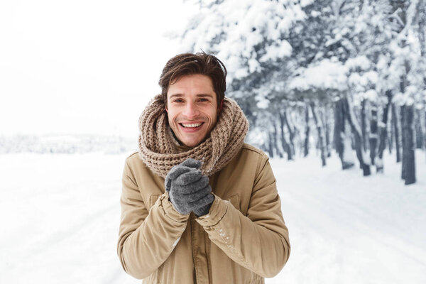 Smiling Man Rubbing Hands In Gloves Standing In Snowy Park