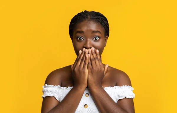 Choqué afro-américain femelle couvrant la bouche avec les mains, posant sur fond jaune — Photo