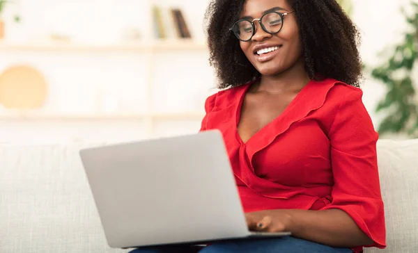 Glückliche schwarze Frau sitzt auf Sofa und benutzt Laptop — Stockfoto