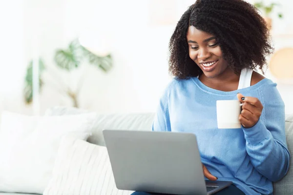 Jovem mulher negra usando laptop sentado no sofá — Fotografia de Stock