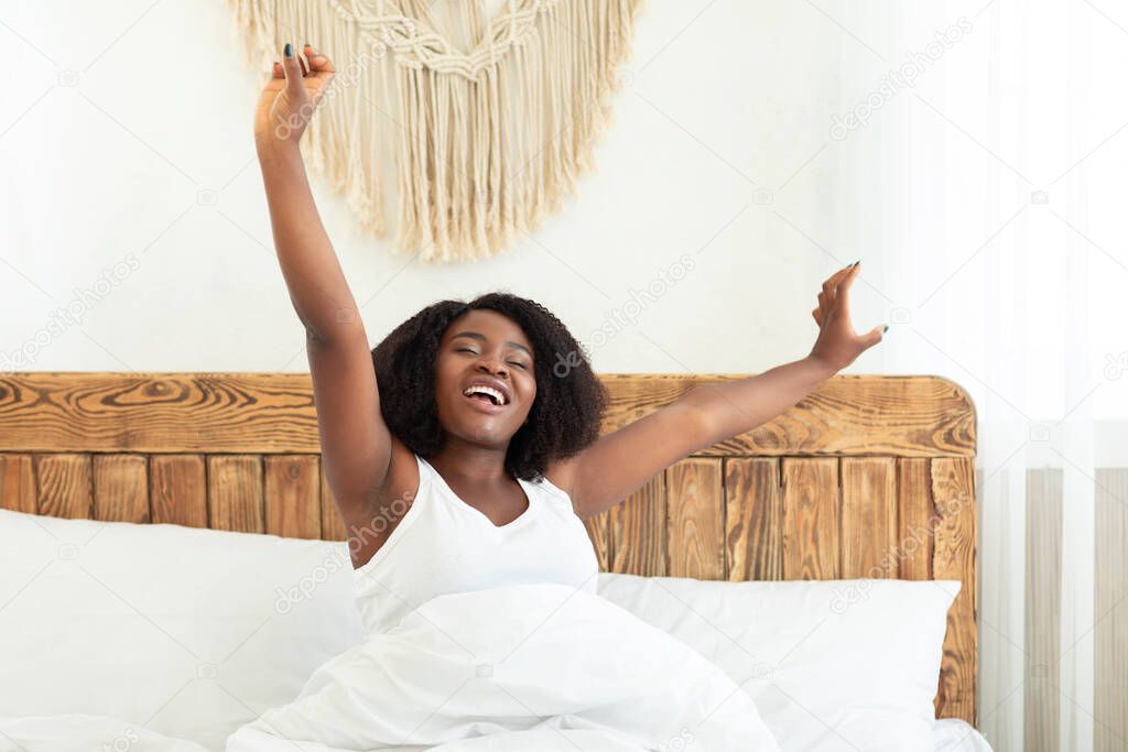 Young happy black lady model stretching sitting in bed