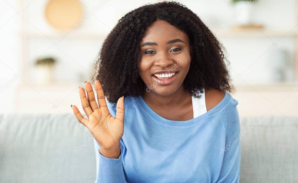 Black woman sitting at home on the sofa and waving
