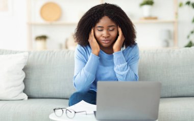 Yorgun siyahi kadın şakaklara dokunup masaj yapıyor.