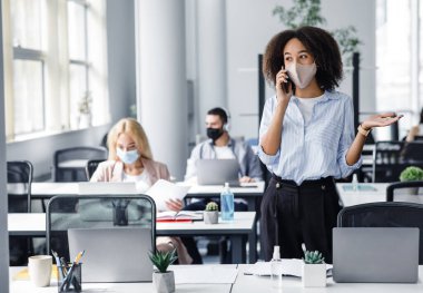 İş yerinde müşteriyle konuşmak ve karantinadan sonra geri dönmek. Çalışanlar ofiste dizüstü bilgisayarlar ve antiseptiklerle çalışıyorlar. Afro-Amerikan kadınlarına odaklanıyorlar.