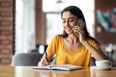 Kafede çay içerken akıllı telefondan konuşan genç bayan.