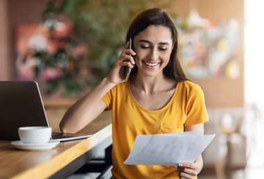 Mutlu Arap kadın telefonda konuşuyor, elinde belgeler var.