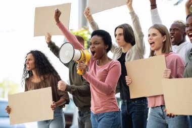 Çok ırklı göstericiler ellerinde megafon ve pankartlarla sokaklarda gösteri yapıyorlar.