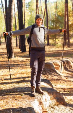 Yürüyen sopalarla ormanda poz veren neşeli bir sırt çantalı.