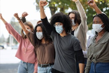 Koruyucu yüz maskesi takan öğrenciler protesto ediyor ve yumruklarını kaldırıyorlar.