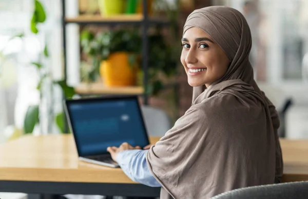 Smiling muslim lady in headscarf working online at cafe