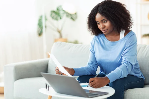 Black woman writing report working on laptop at home