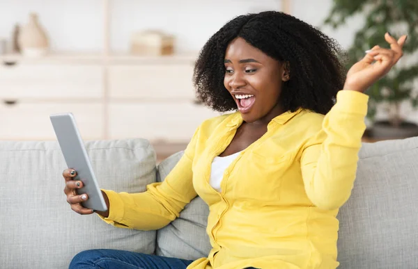 Donna nera seduta sul divano, utilizzando tablet — Foto Stock