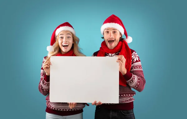 Christmas ad. Excited millennial couple holding empty poster with mockup for design on blue background — Stock Photo, Image