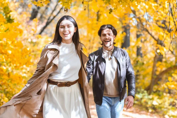 Mladý muž a žena běží podzimním lesem, drží se za ruce — Stock fotografie