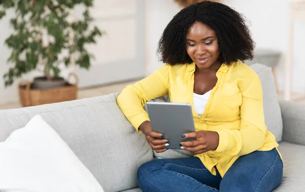 Donna nera seduta sul divano, utilizzando tablet — Foto Stock