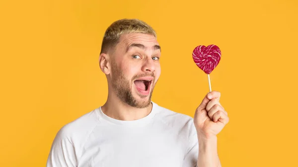 Homem emocional com boca aberta detém pirulito do coração — Fotografia de Stock
