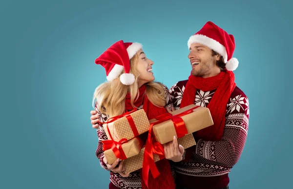 Портрет люблячої тисячолітньої пари в зимових вбраннях, що тримає купу різдвяних подарунків на синьому фоні, порожній простір — стокове фото