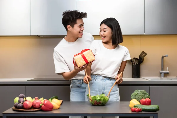 Loving Chinese Husband Giving Wife Wrapped Gift Standing In Kitchen — Stock Photo, Image