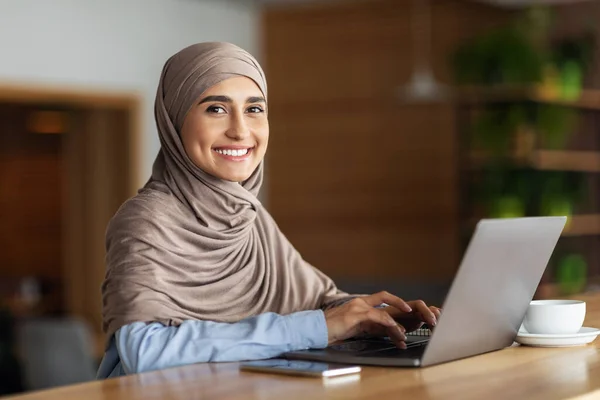 Веселая мусульманка в хиджабе работает онлайн в кафе — стоковое фото