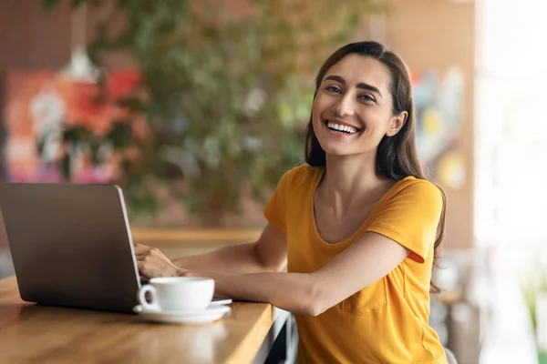 Веселая арабская леди сидит перед ноутбуком в кафе — стоковое фото