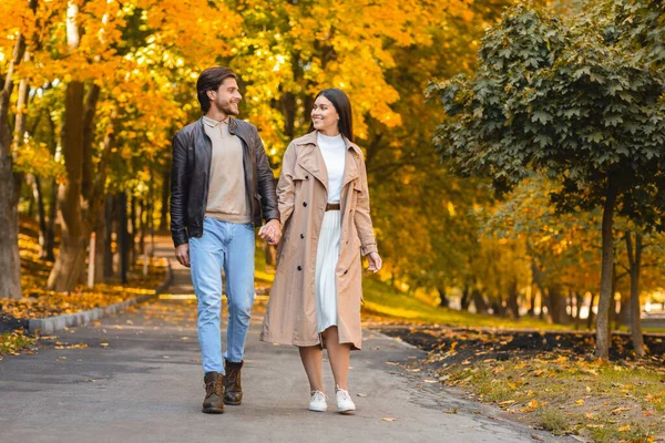 Hombre y mujer positivos tomados de la mano y caminando por el parque —  Fotos de Stock