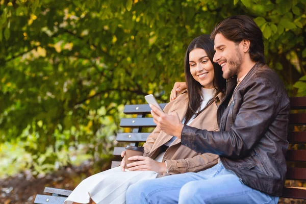 Casal feliz sentado na bech no parque, usando telefone celular — Fotografia de Stock